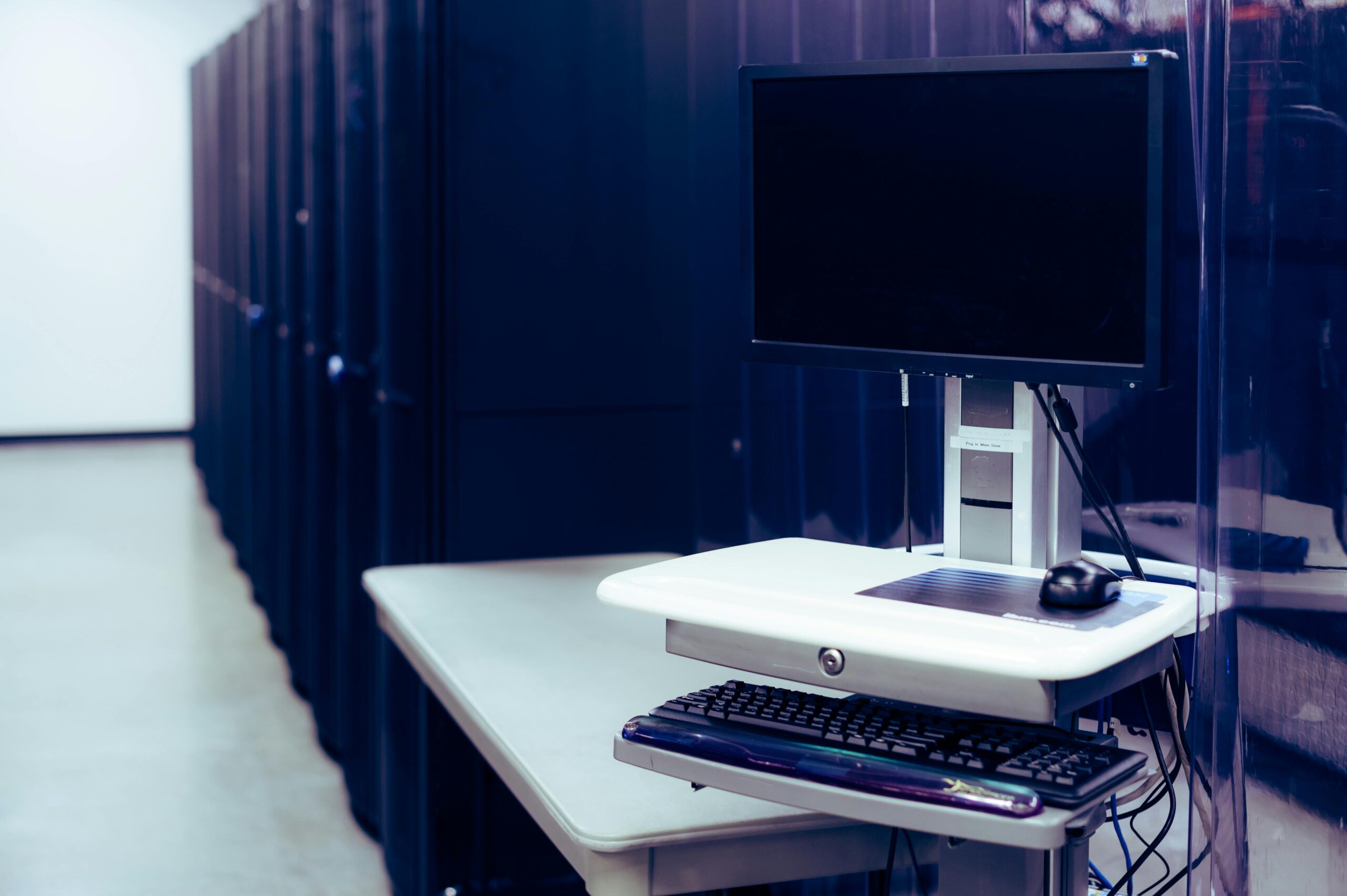 Contemporary computer with black screen placed on stand near row of server steel racks in data center